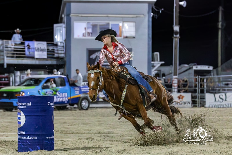 Cowgirl in pink sparkle shirt on chestnut horse rounding barrel