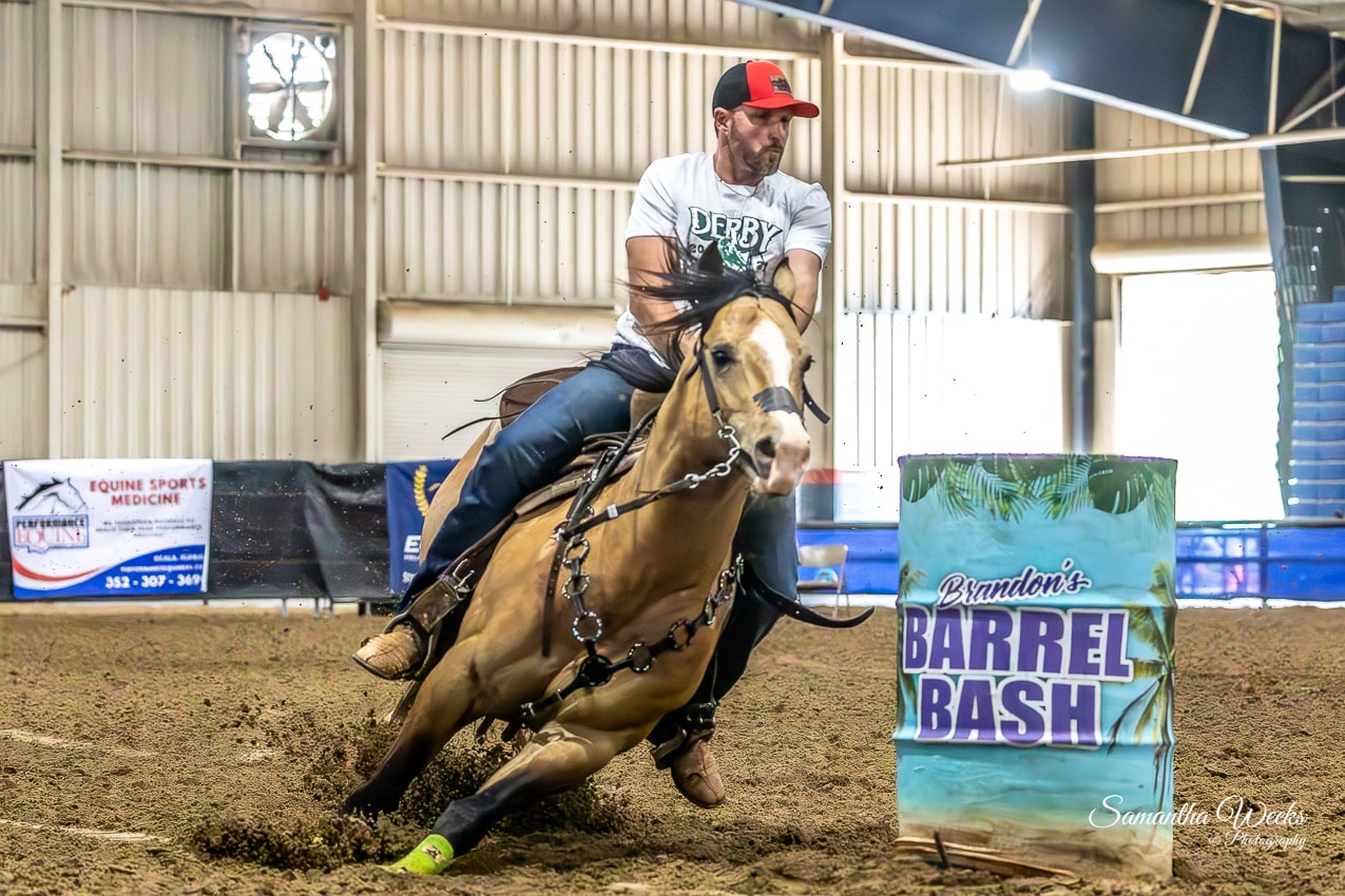 Man in Derby shirt and red cap on buckskin horse turning Brandon's Barrel Bash drum