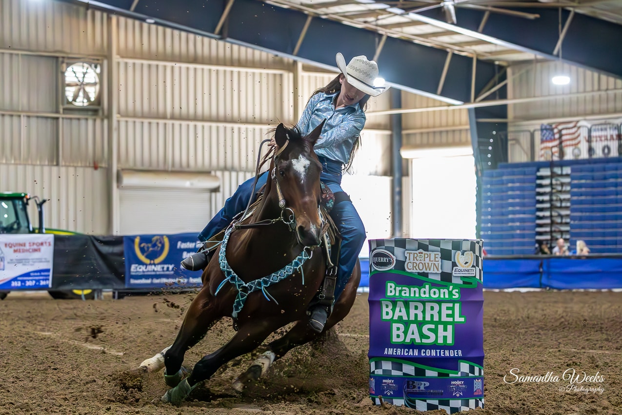 Cowgirl in blue shirt on dark bay horse with teal breast collar rounding barrel