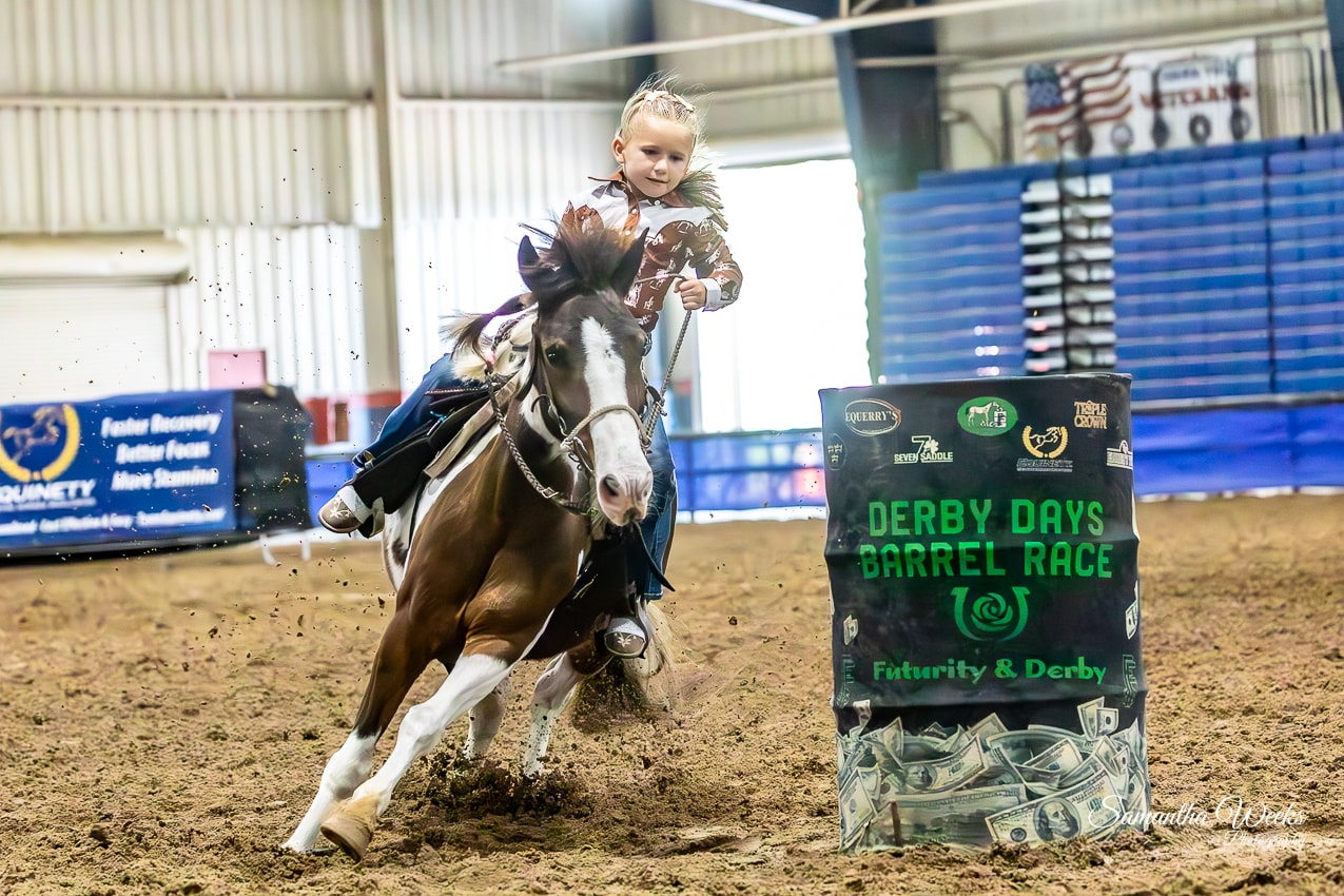 Young girl in western shirt on paint pony rounding Derby Days Barrel Race drum