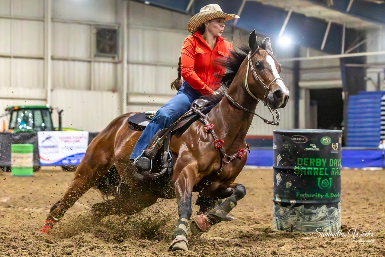 Cowgirl in orange shirt on bay horse rounding Derby Days Barrel Race drum