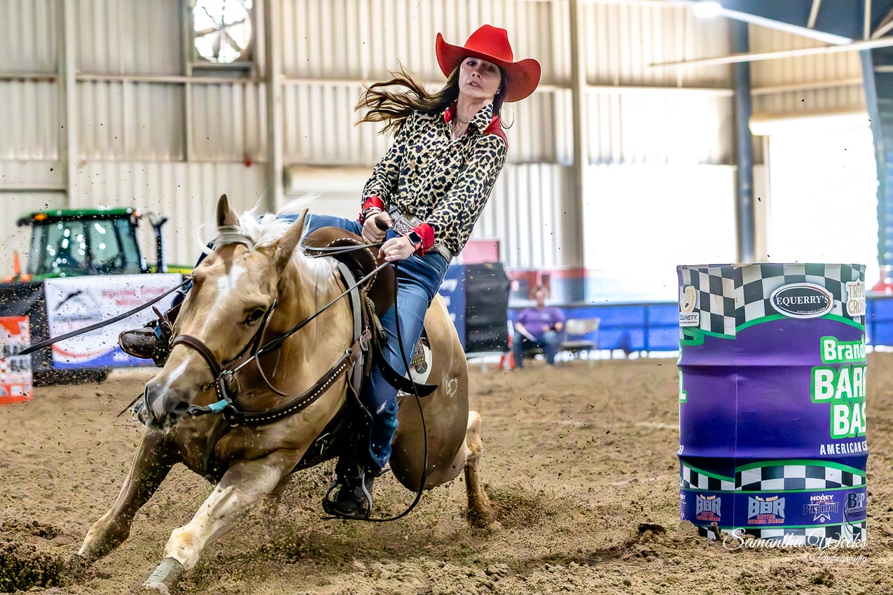 Cowgirl in leopard print shirt and red hat on palomino horse rounding Brandon's Barrel Bash drum