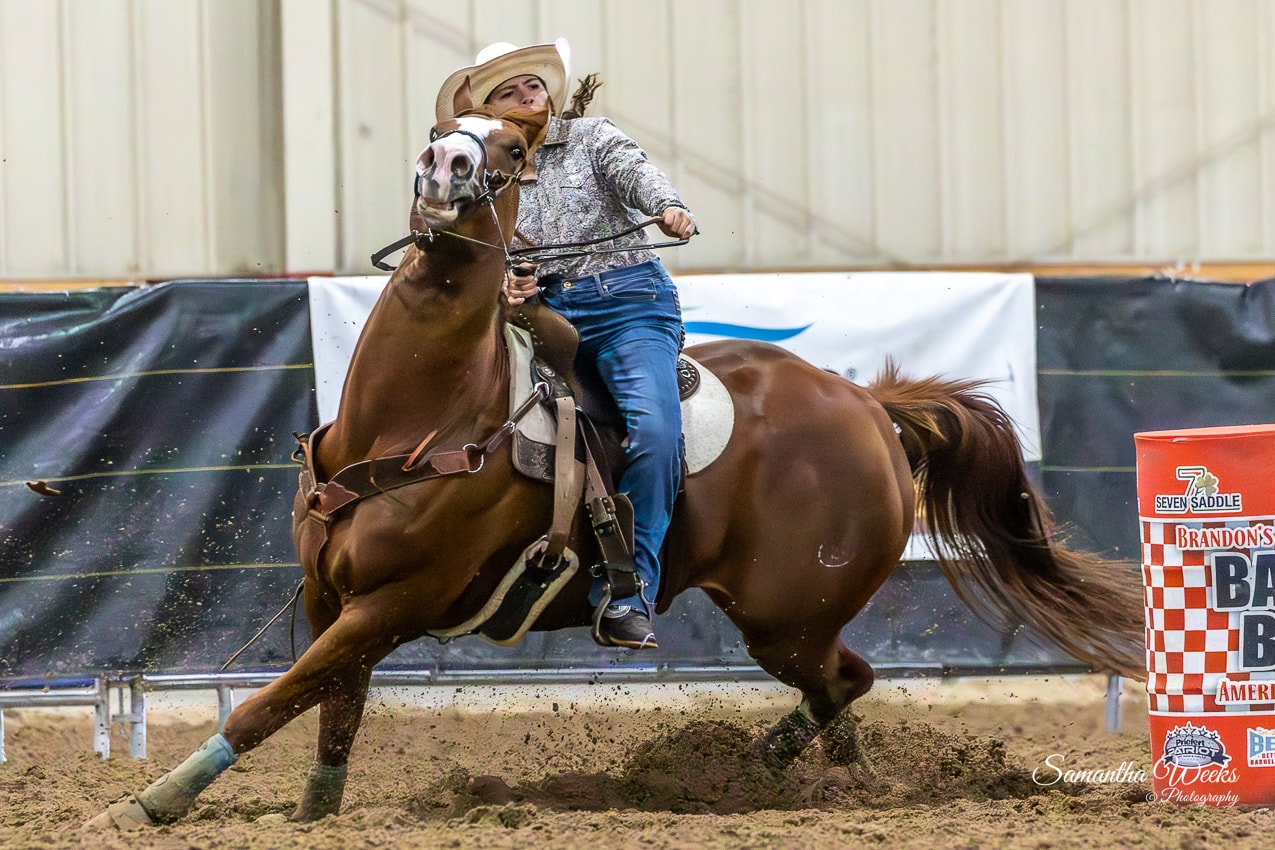 Cowgirl in floral shirt on chestnut horse rounding Brandon's Barrel Bash drum