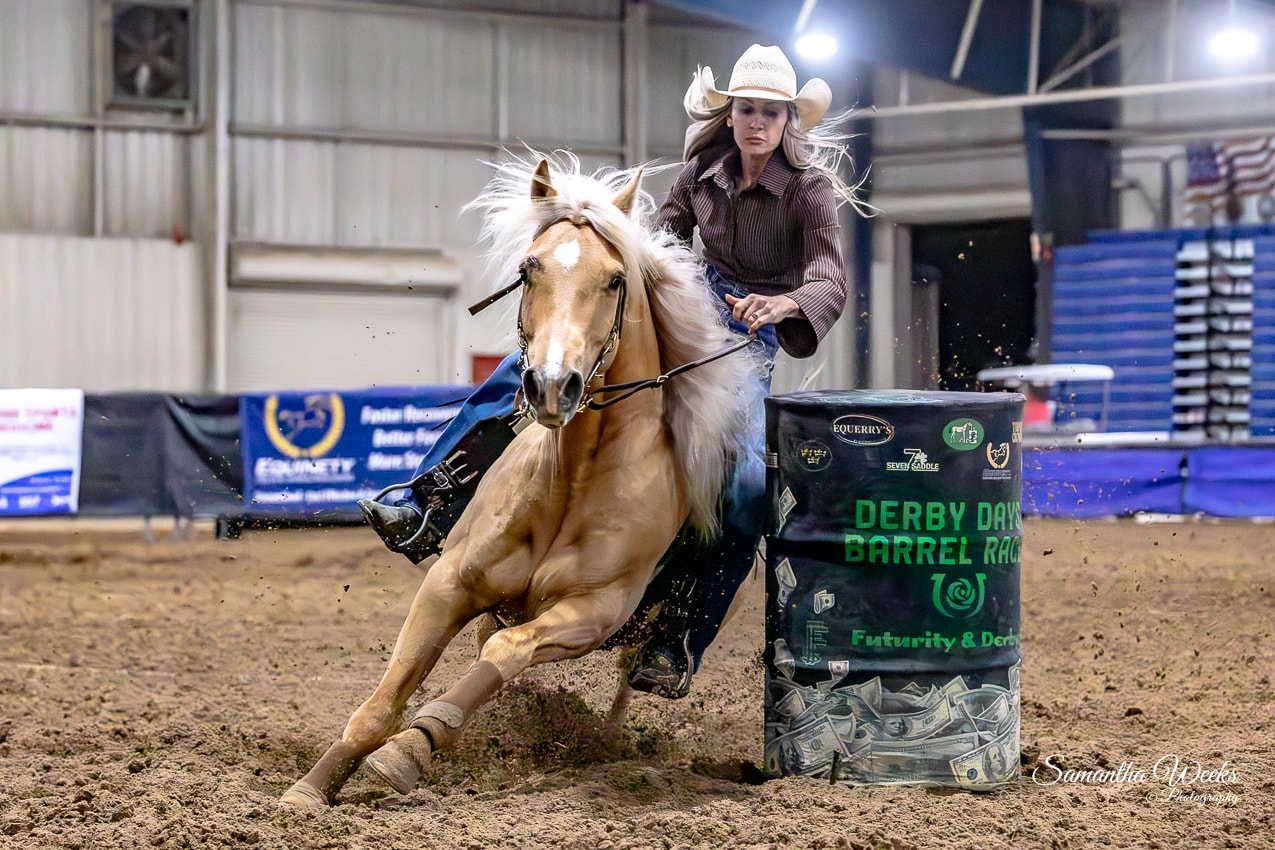 Cowgirl in brown shirt on palomino horse with flowing mane rounding Derby Days Barrel Race drum