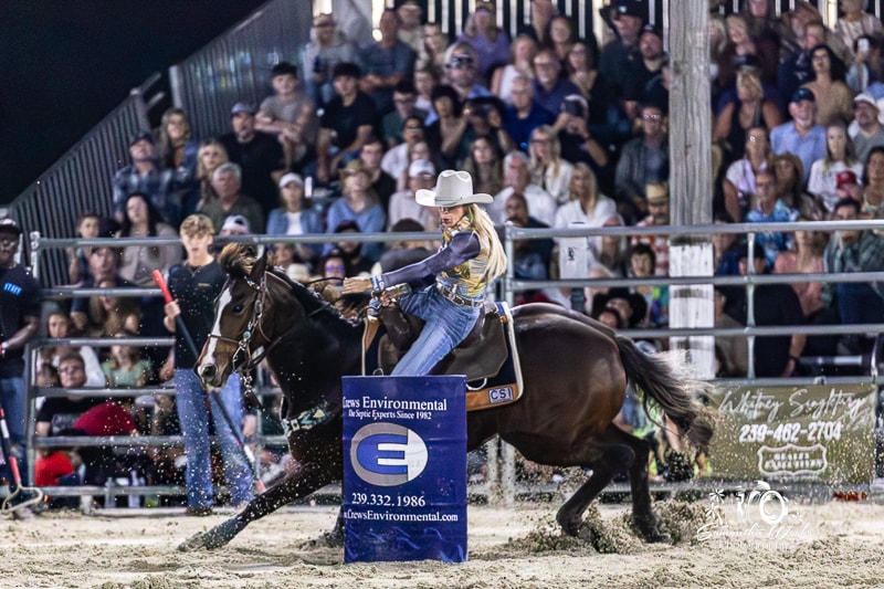 Cowgirl in white hat leaning into barrel turn packed arena crowd