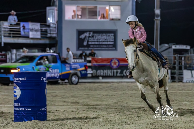 Young girl in pink helmet on grey horse rounding barrel
