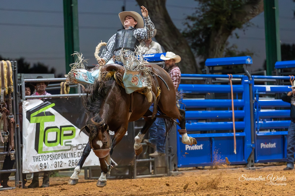 Bronc rider on bucking horse outdoor arena Top Shop banner daytime