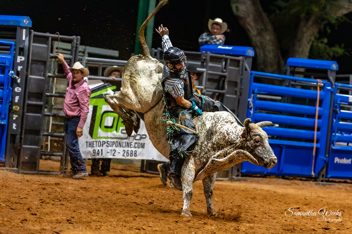 Bull rider on white bull spinning near Top Shop banner outdoor arena