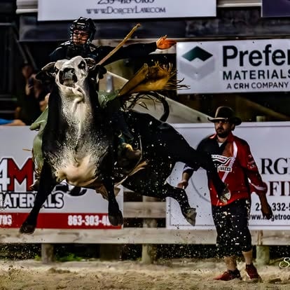 Bull rider on black and white bull with bullfighter nearby