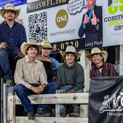 Group of young cowboys seated on arena fence smiling