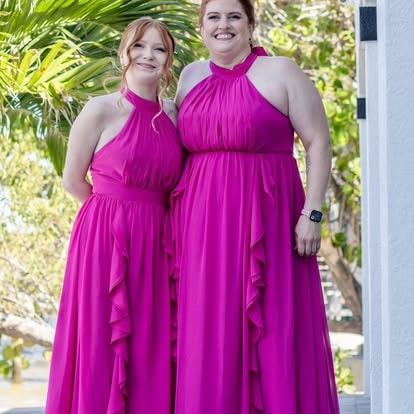 Two women in magenta halter dresses smiling